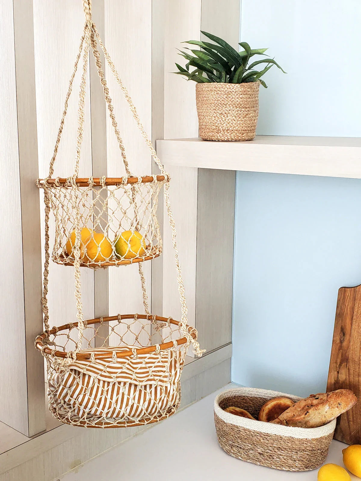 Double hanging macrame basket with lemons and pillow beside woven basket with bread on kitchen countertop