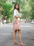 Woman in white dress carrying red striped jute tote bag with tassel on tree-lined street