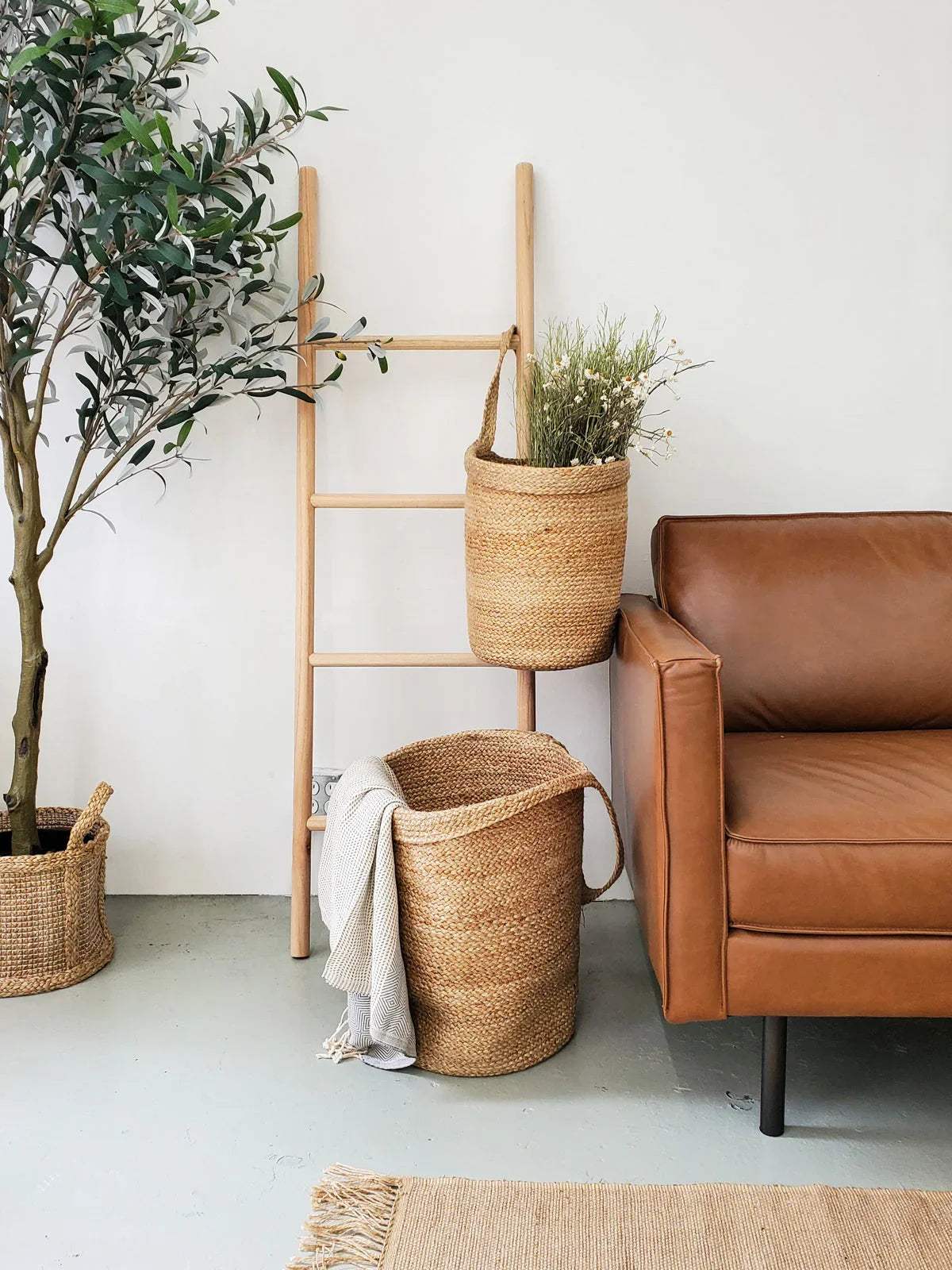 Natural woven baskets on a wooden ladder next to a tan leather sofa in a cozy living space