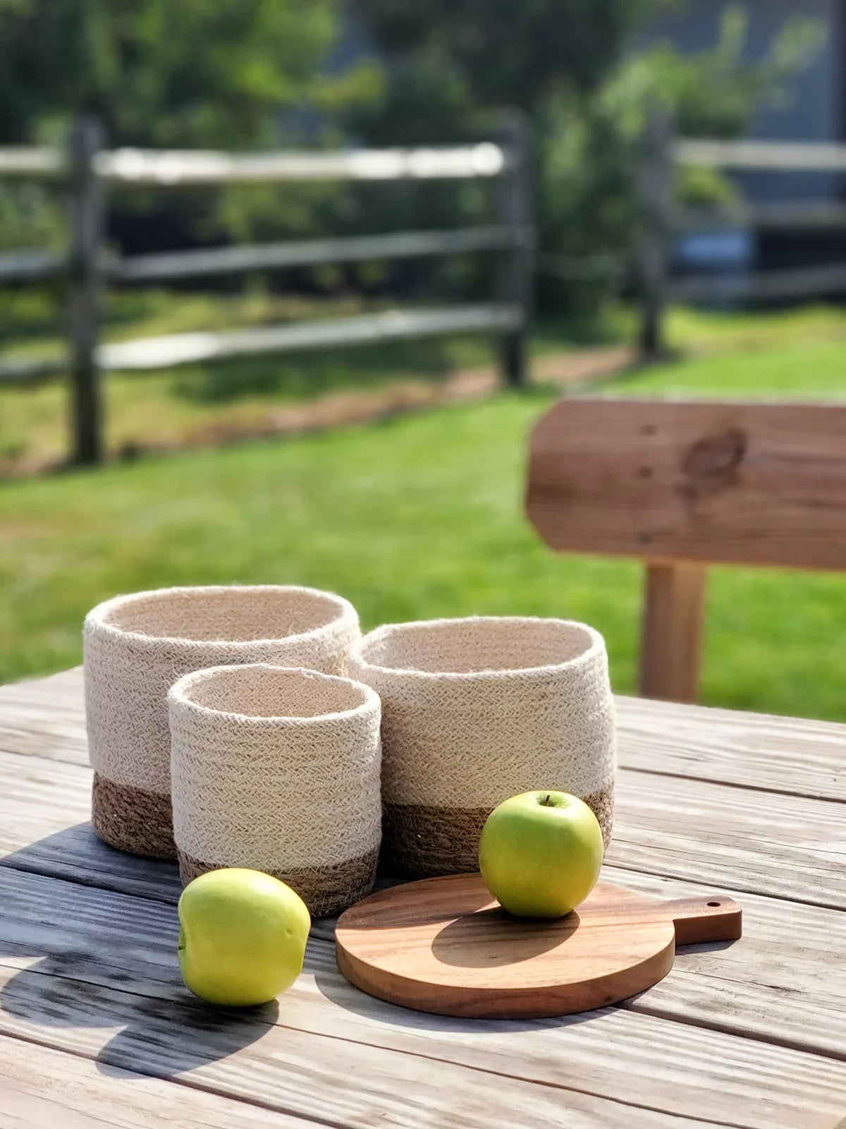 Set of three woven storage baskets with beige and brown design on wooden table outdoors with green apples