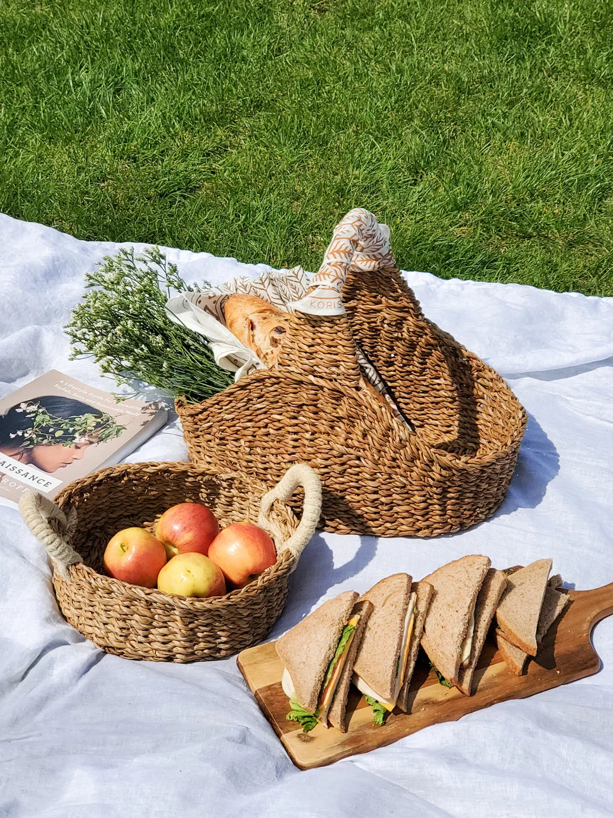 Eco-friendly woven baskets for picnic, with apples, bread, and sandwiches on a blanket outdoors