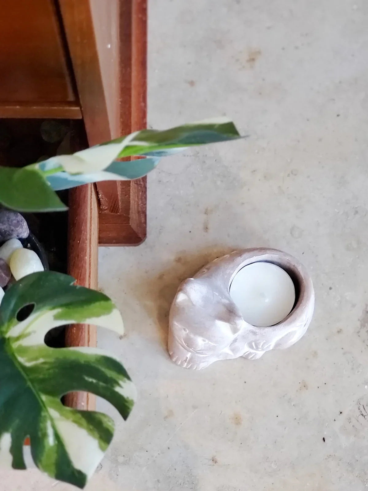 Terracotta cat-shaped candle holder with white tealight on beige surface near green variegated plant