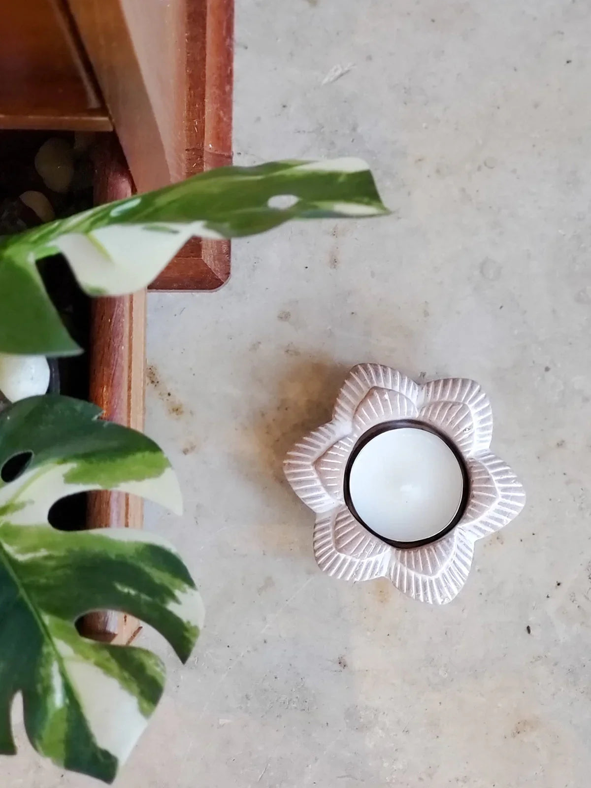 Terracotta flower-shaped candle holder with white candle on marble surface near green variegated leaves