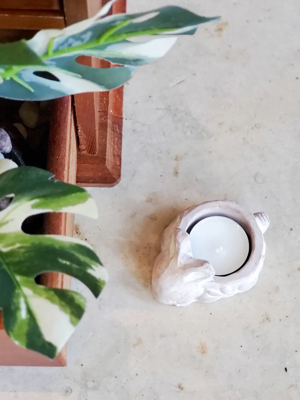 Terracotta rabbit-shaped candle holder with white tealight on light stone surface next to green variegated leaves