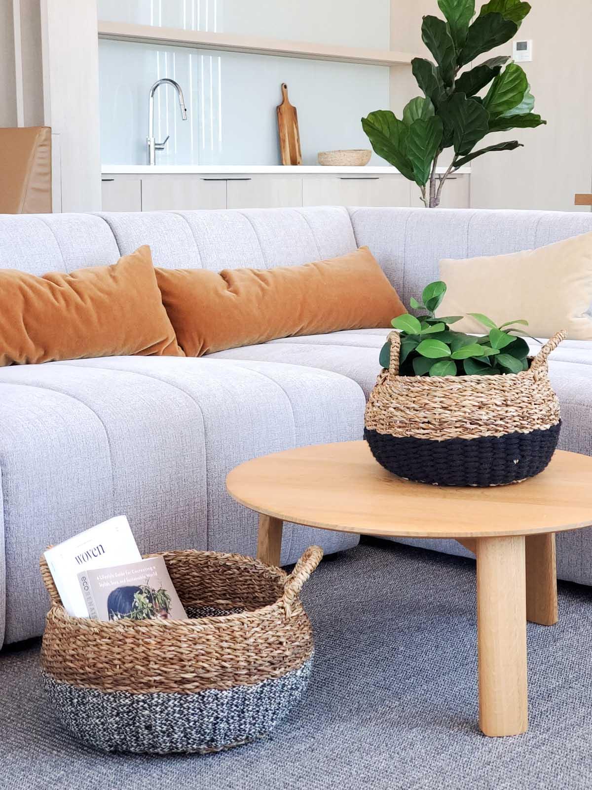 Modern living room with gray sectional sofa, mustard pillows, round wooden coffee table, and two woven baskets