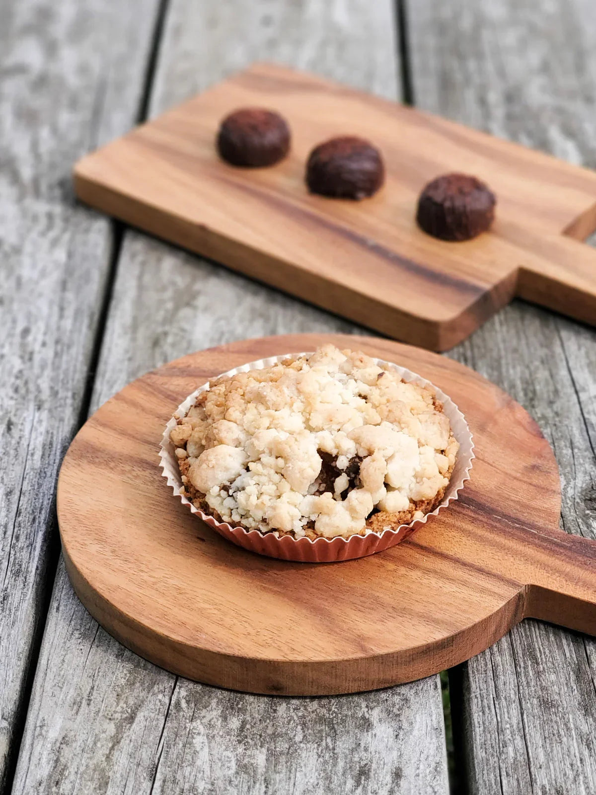 Crumb-topped tart on round wooden serving board, three chocolate truffles on rectangular board, rustic wood table