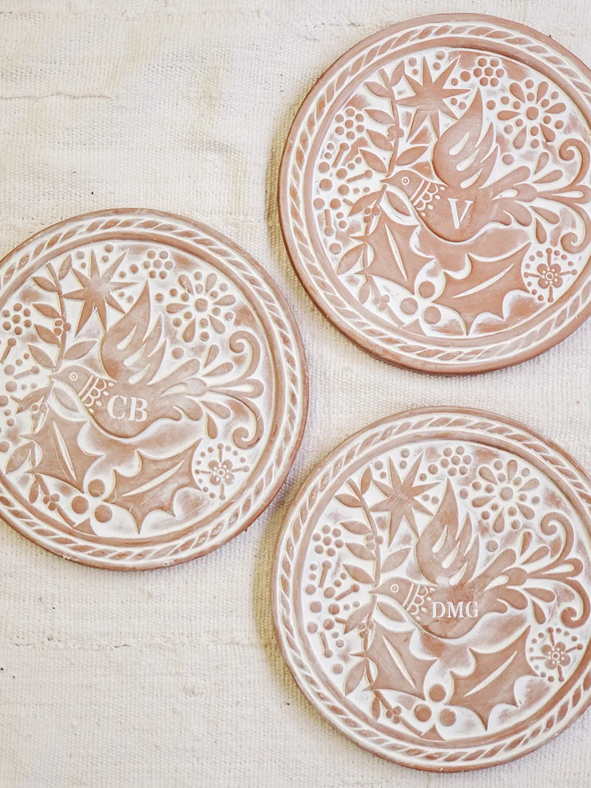Three round monogrammed bread warmer baskets with bird and floral patterns on beige fabric