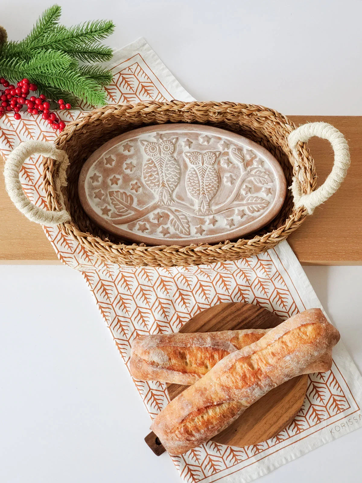 Oval woven bread warmer basket with rope handles and ceramic owl design, rustic table setting with baguettes