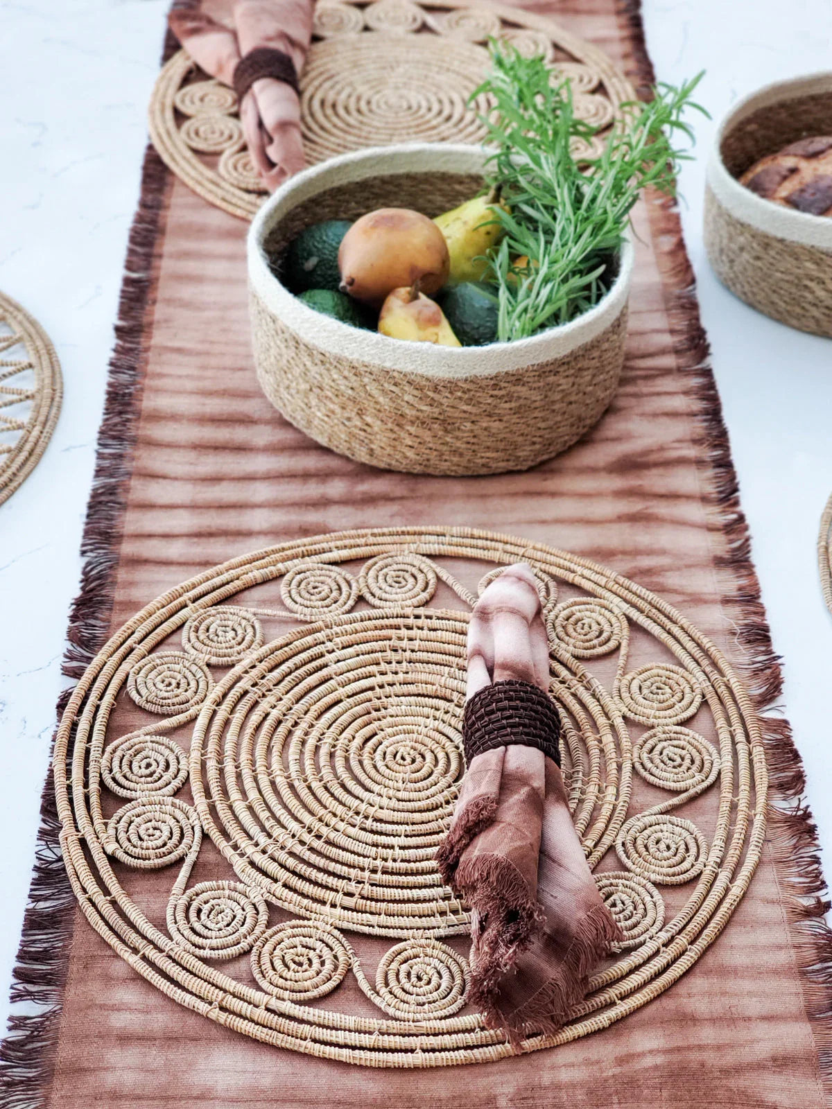 Natural woven palm fiber placemat set with rustic napkin and basket holding fruits and herbs on table runner