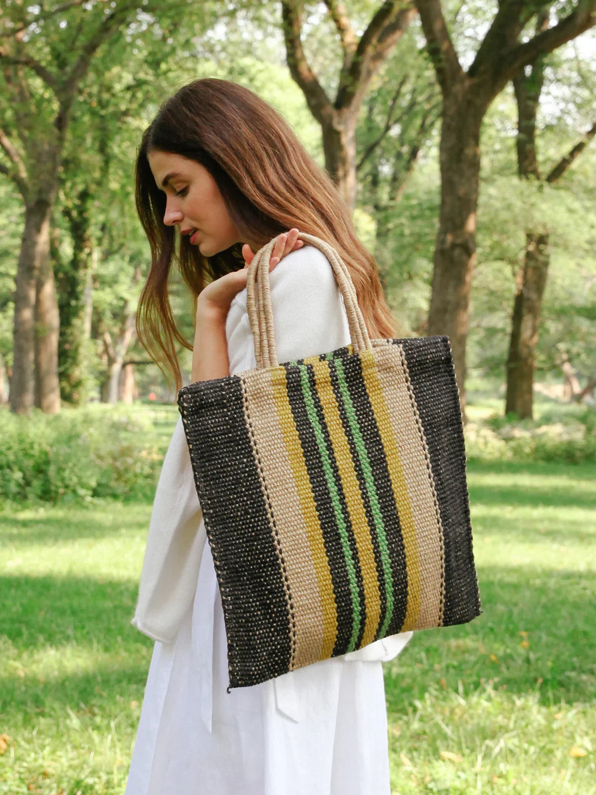 Woman in white dress carrying woven tote bag with black, beige, green, and yellow stripes in park