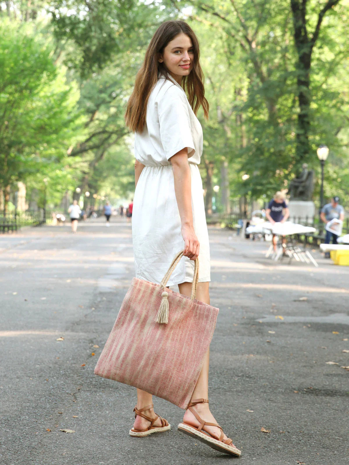 Woman in white dress holding red jute tote bag with rope handles walking in park
