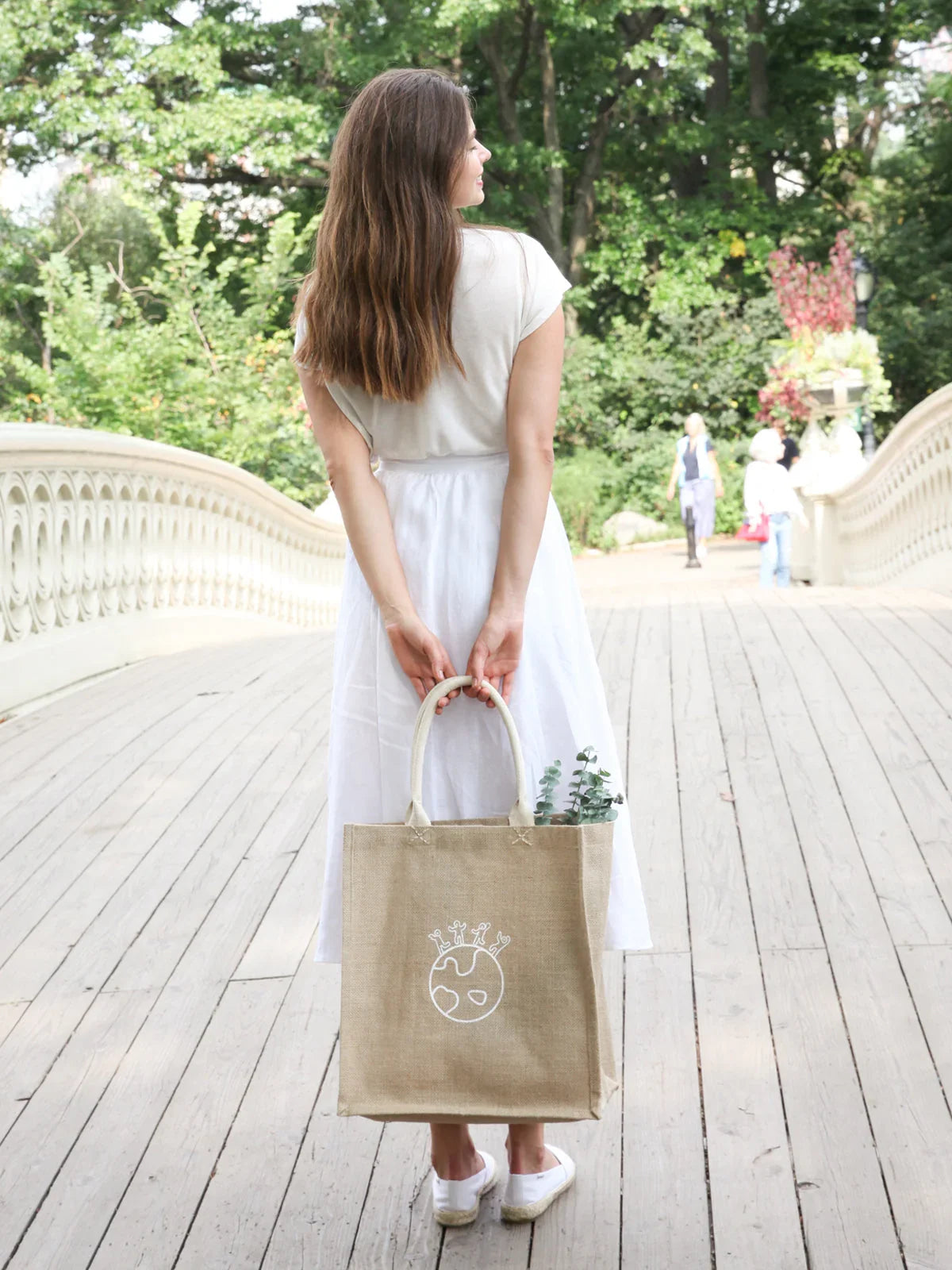 Woman in white dress holding eco-friendly jute tote bag with world design in a park