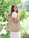 Woman in white dress holding eco-friendly jute market bag with leaf design by green lake