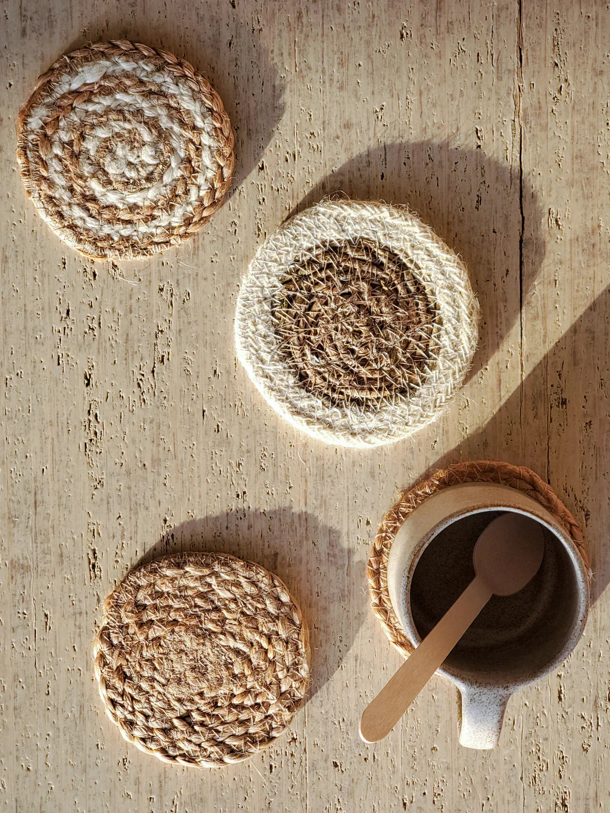 Set of woven round mini coasters in natural tones on rustic wooden table with ceramic cup and wooden spoon