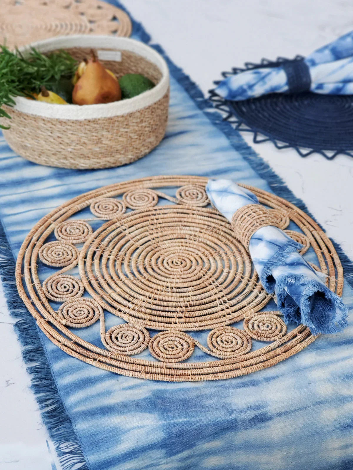 Blue tie-dye table runner with circular woven placemat and matching napkin on marble surface