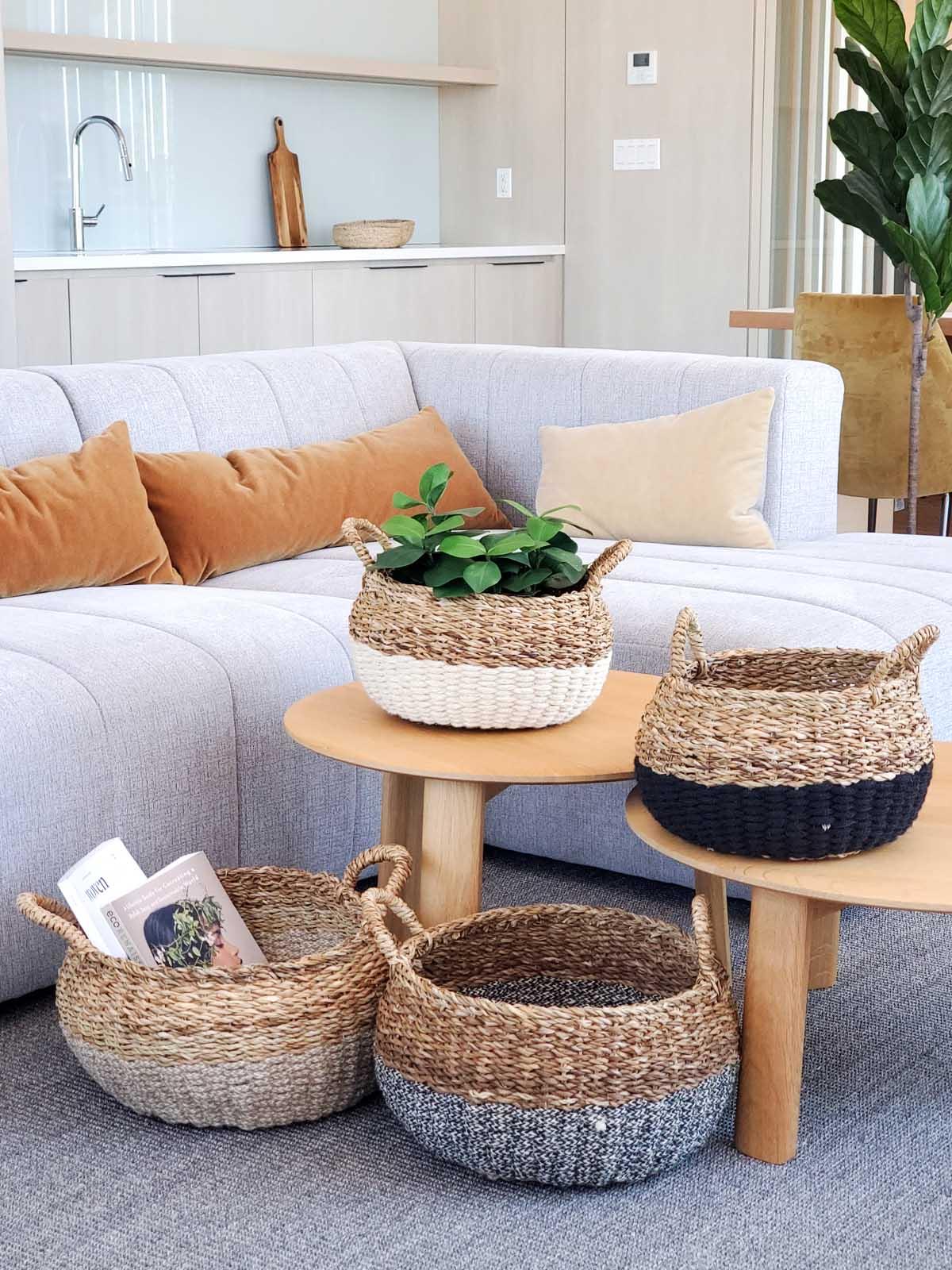 Set of four woven storage baskets with color-block design in modern living room with light sofa and wooden tables