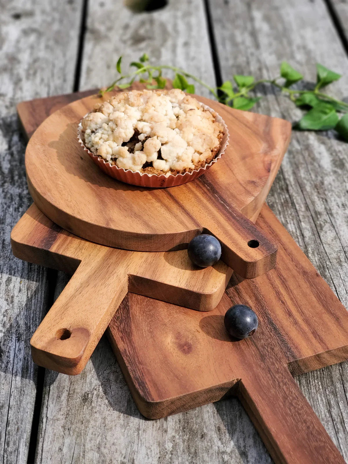 Wooden serving boards with a crumble-topped tart and two blueberries on a rustic wooden table