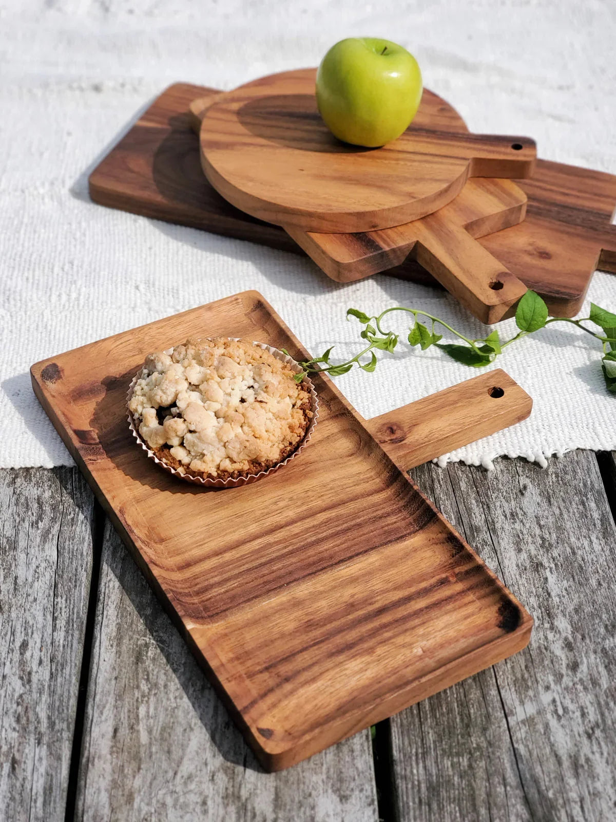 Wooden serving trays with handle, topped with a crumbly muffin and green apple on rustic wooden surface