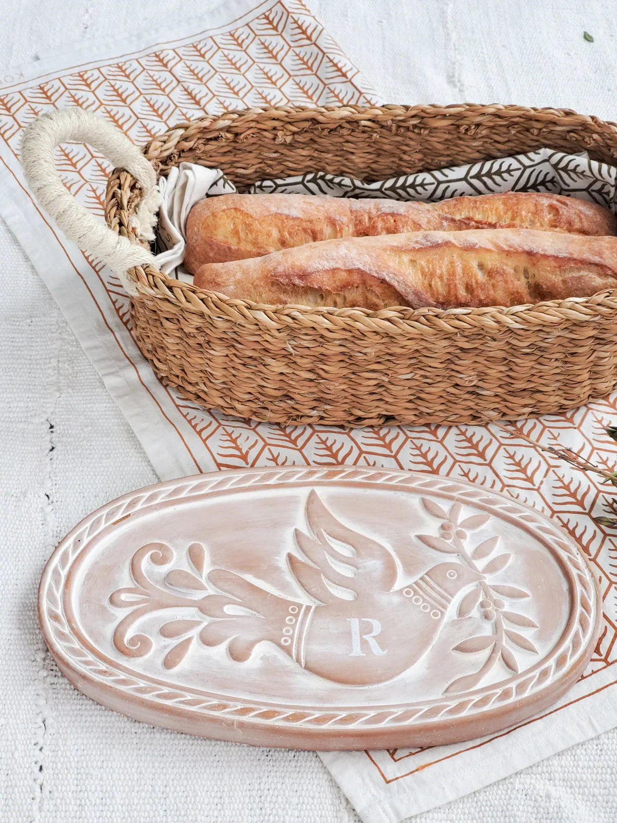 Woven bread warmer basket with two baguettes and a monogrammed oval wooden lid featuring a dove design