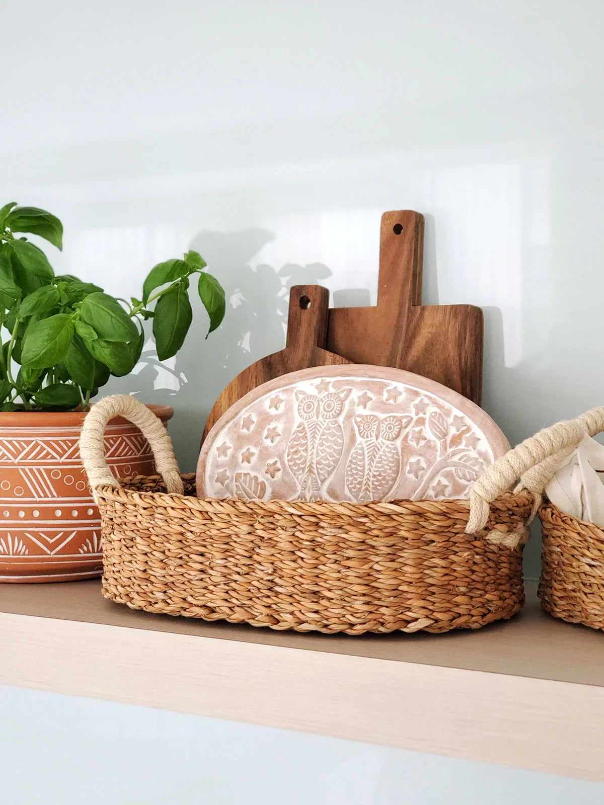 Oval woven bread warmer basket with owl design plate and wooden cutting boards on shelf