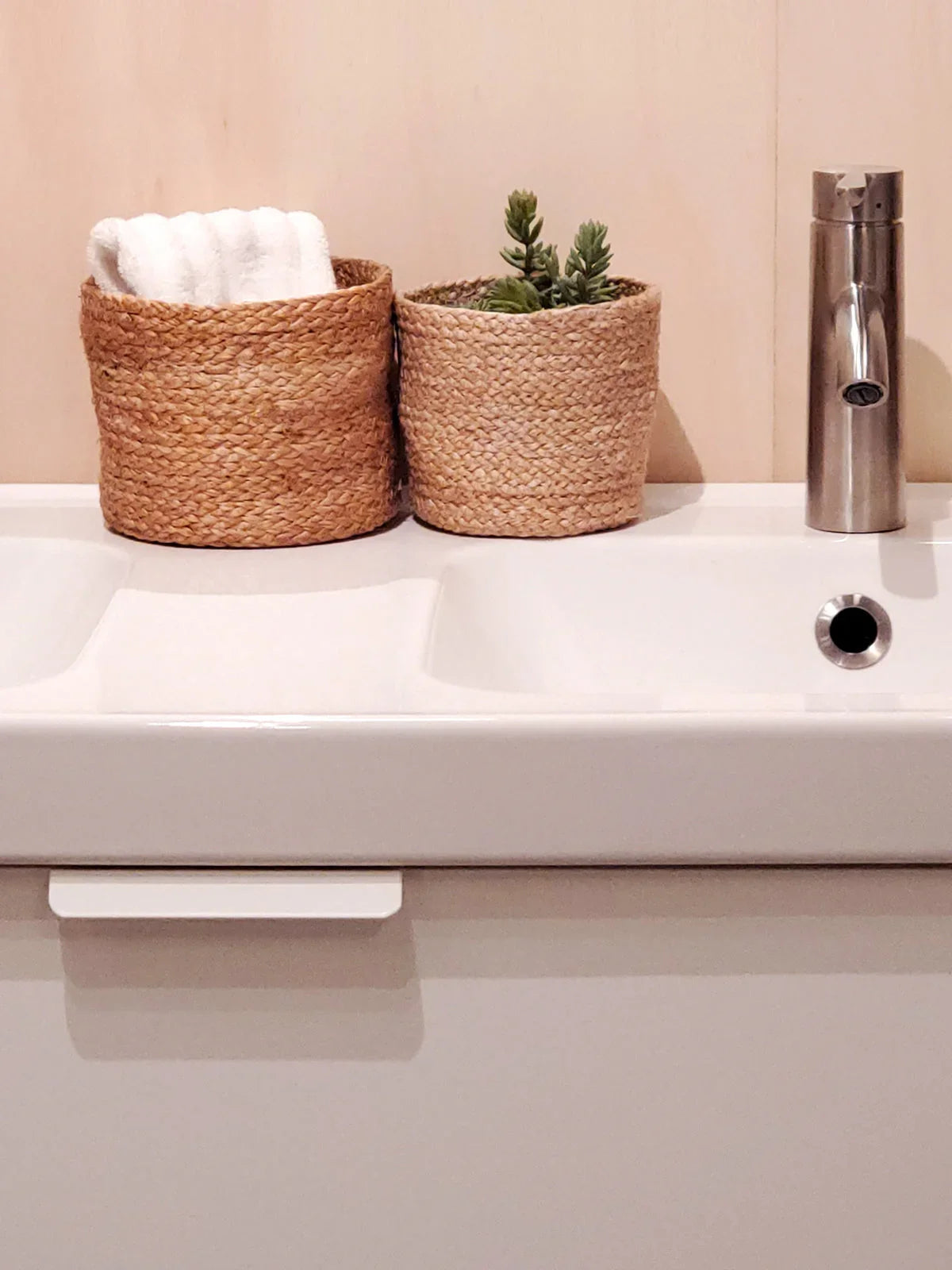 Bathroom sink with two woven baskets, one holding a white towel and the other with green succulents