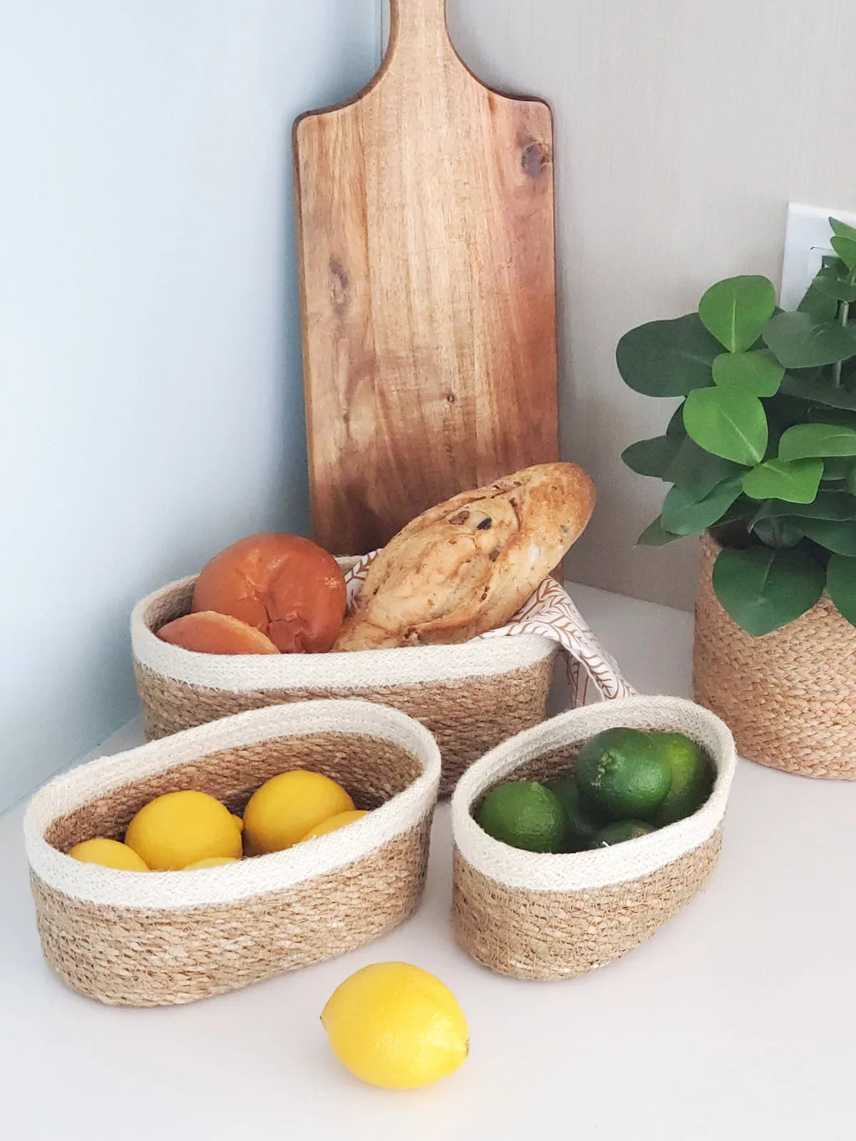 Set of three woven Savaro oval baskets with bread, lemons, and limes on a kitchen countertop