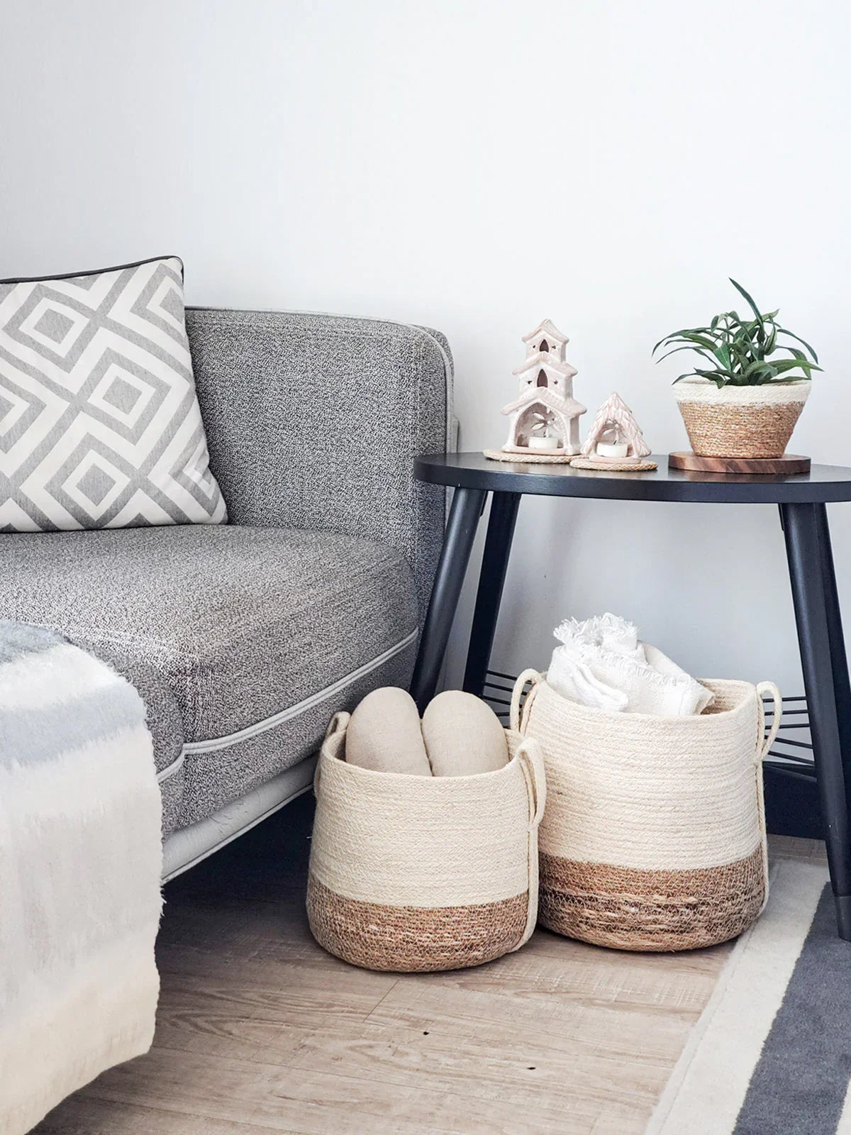 Modern living room corner with gray sofa, side table, woven storage baskets and decorative items