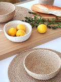 Natural woven placemats and bowls on wooden surface with lemons, bread, and green leaves