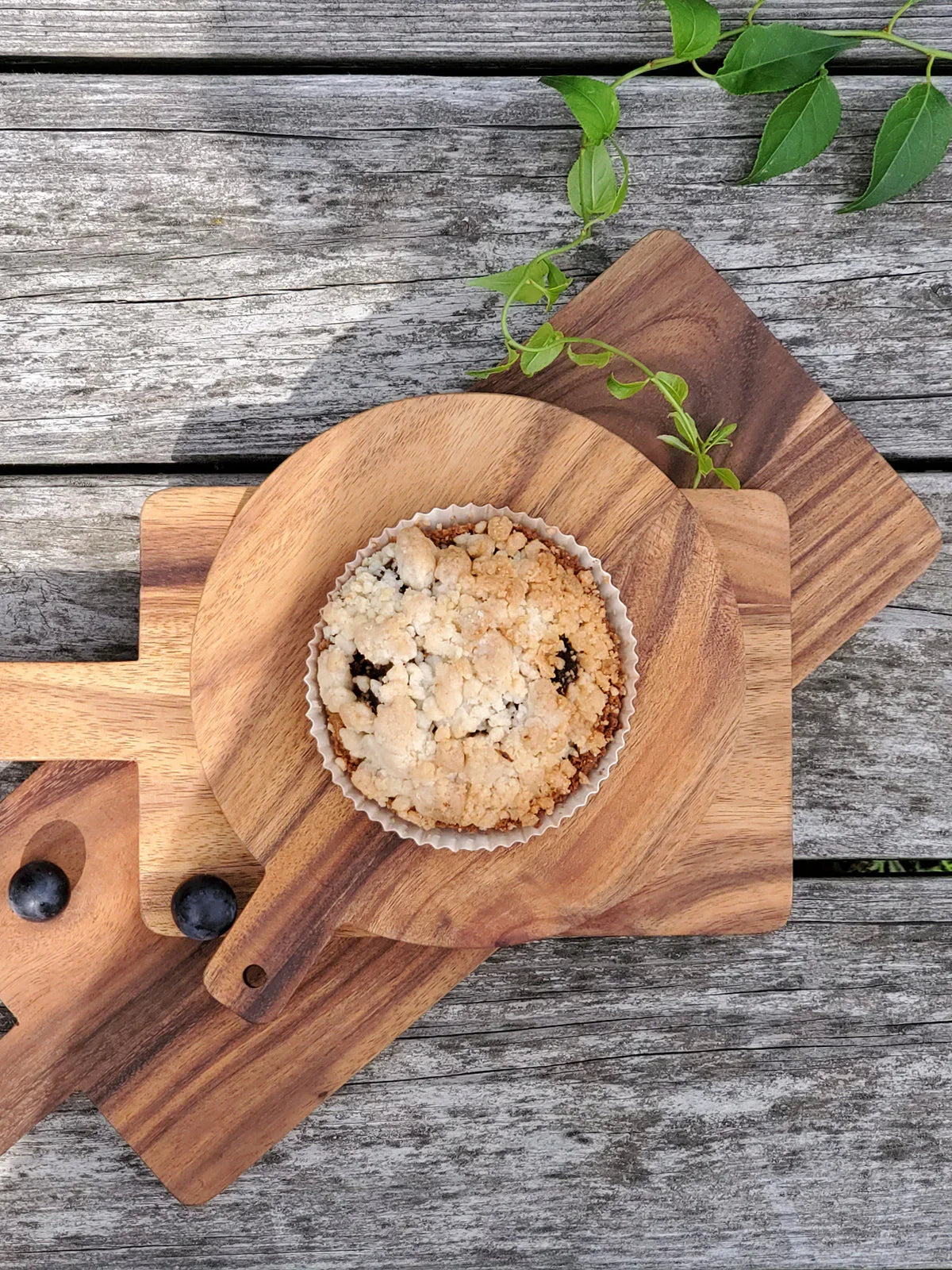Blueberry crumble tart on round wooden serving board with two blueberries on rustic wooden table