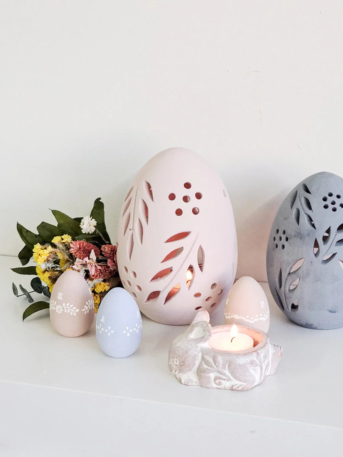 Decorative egg-shaped candle lanterns in pastel colors with floral cutouts, lit tea light, and dried flowers