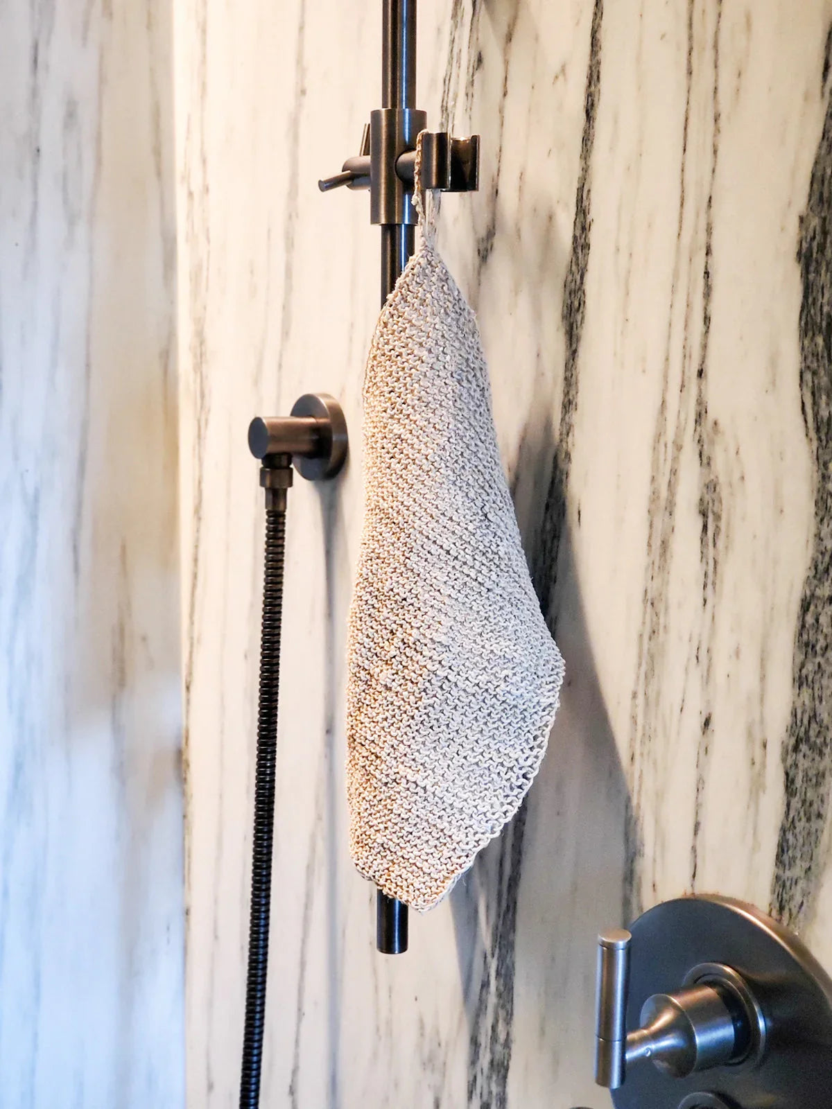 Knitted hemp washcloth hanging on black shower fixture in a marble bathroom