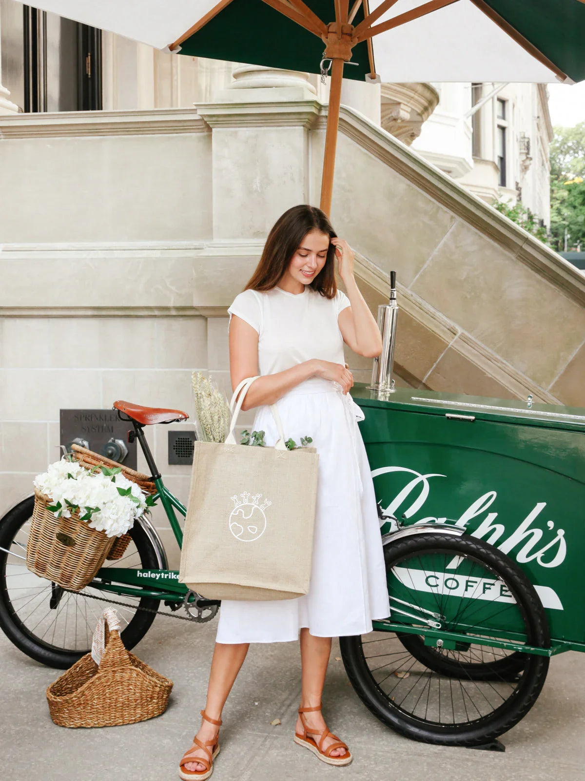 Woman with earth print jute market bag in front of a green coffee cart, summer outfit, Qu!rk Boutique