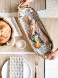 Oval woven bread basket with two baguettes and a small orange on patterned cloth, on a rustic table setting