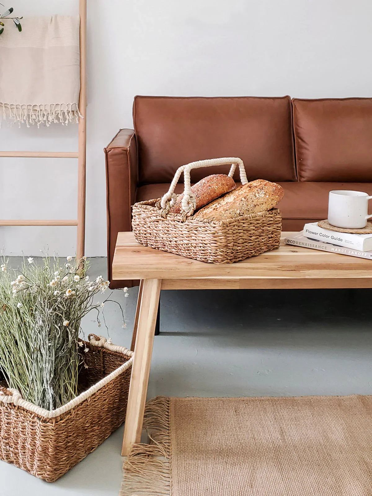Woven storage basket with handles holding bread on wooden table in modern living room with brown leather sofa