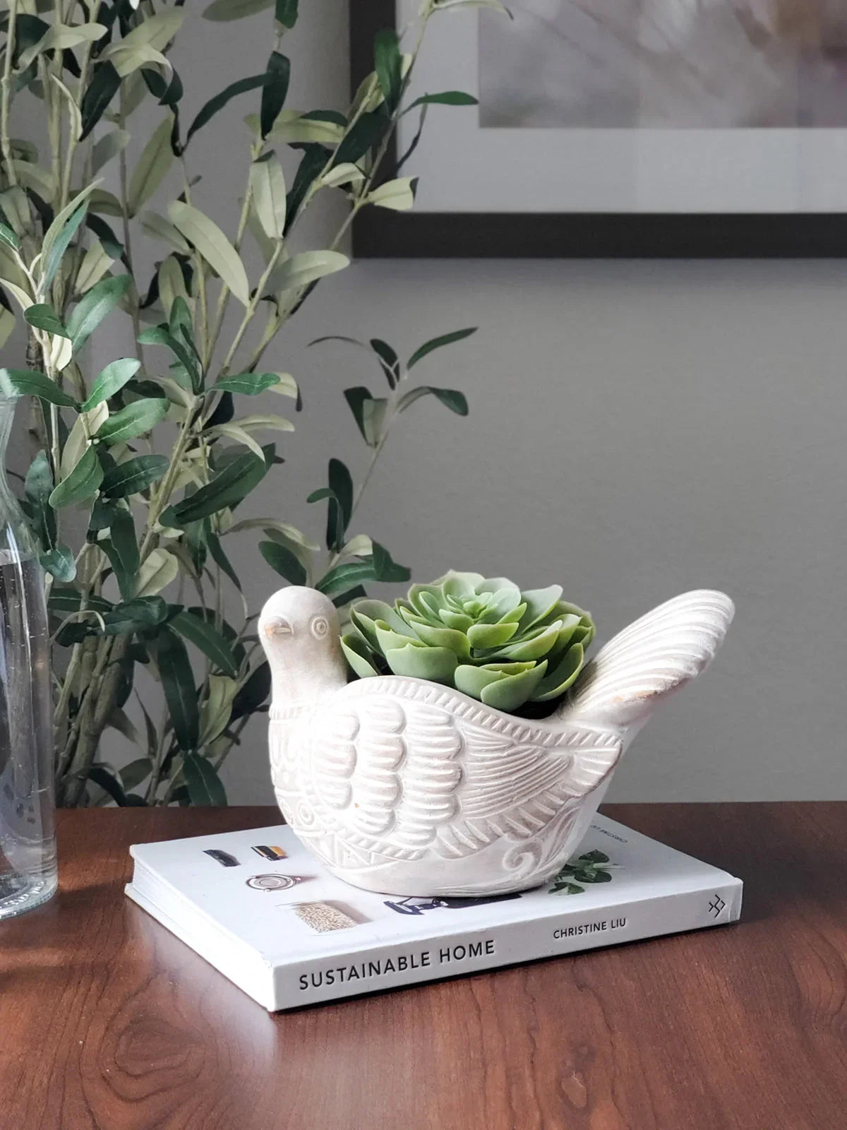 White ceramic dove-shaped planter with green succulent on book titled Sustainable Home