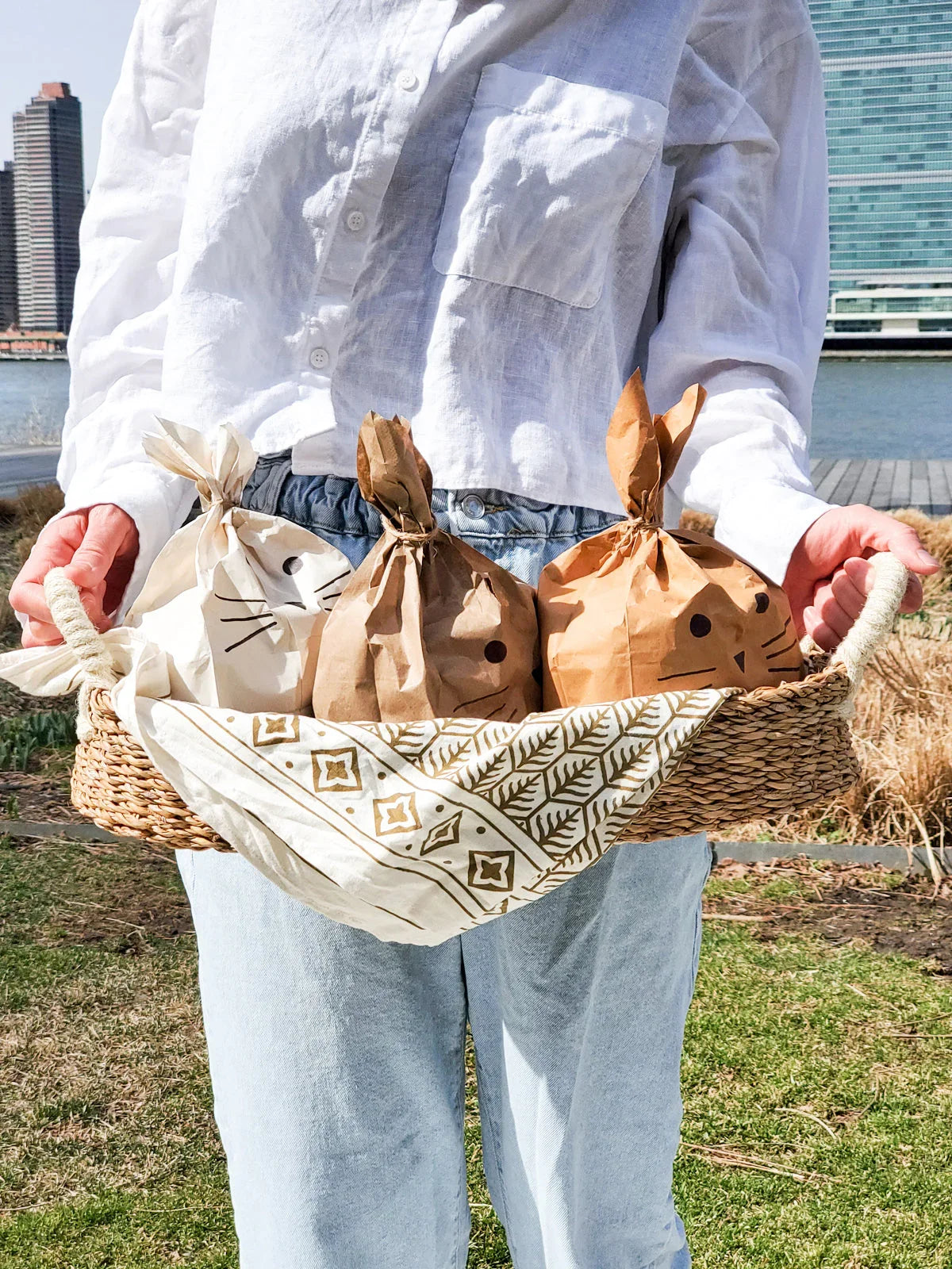 Person holding woven bread basket with white handles, containing three animal face paper bags outdoors
