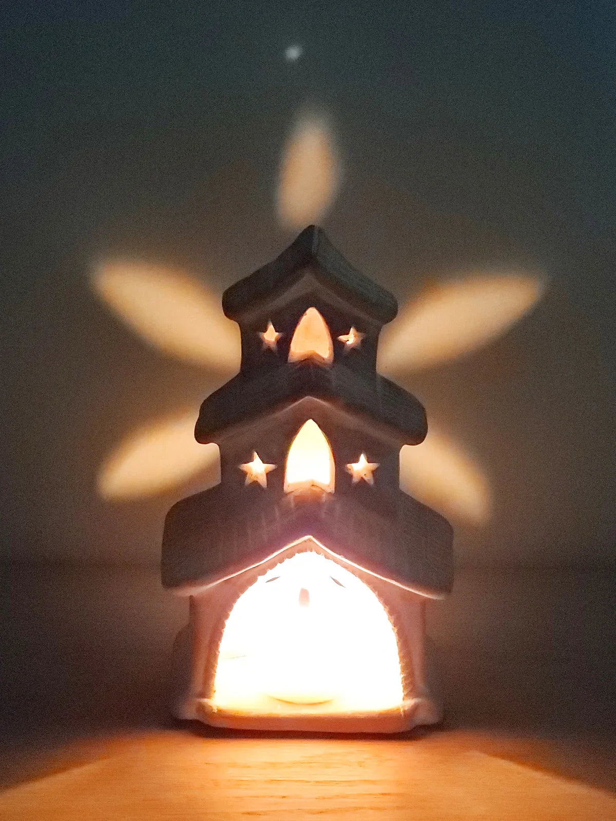 Terracotta candle holder shaped like a house with star-shaped light openings casting warm light patterns