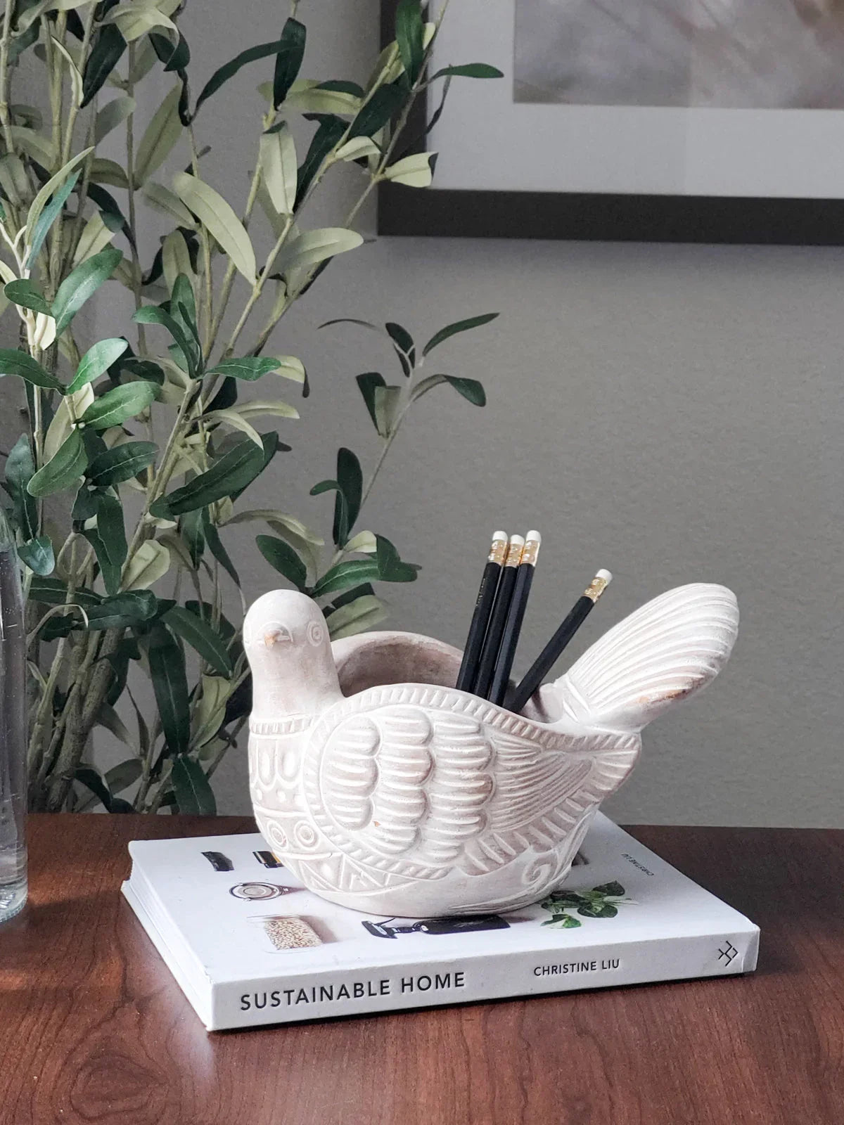 White ceramic bird planter holding pencils on Sustainable Home book with green plant background