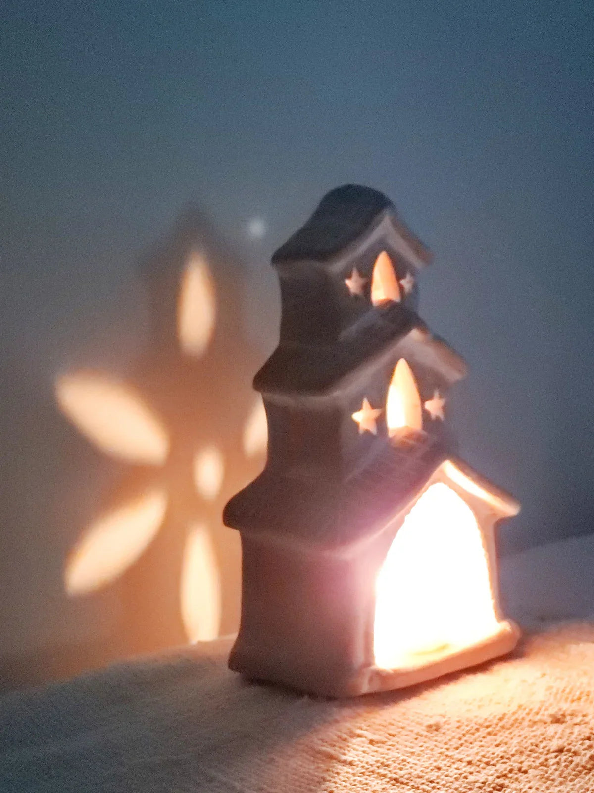 Glowing terracotta candle holder shaped like a house casting star-shaped light on wall