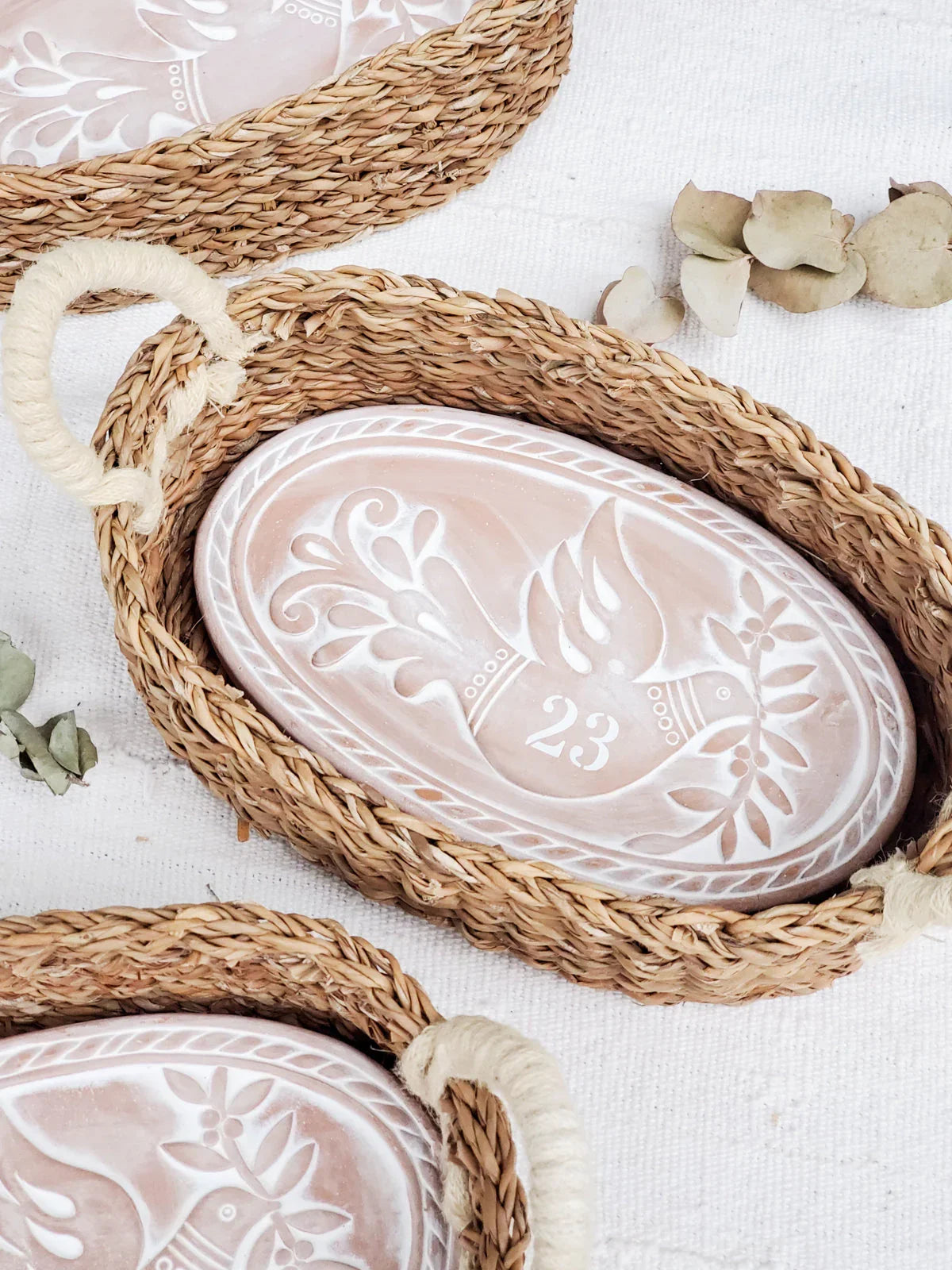 Oval ceramic bread warmer with bird and number 23 design in woven rattan basket on white fabric