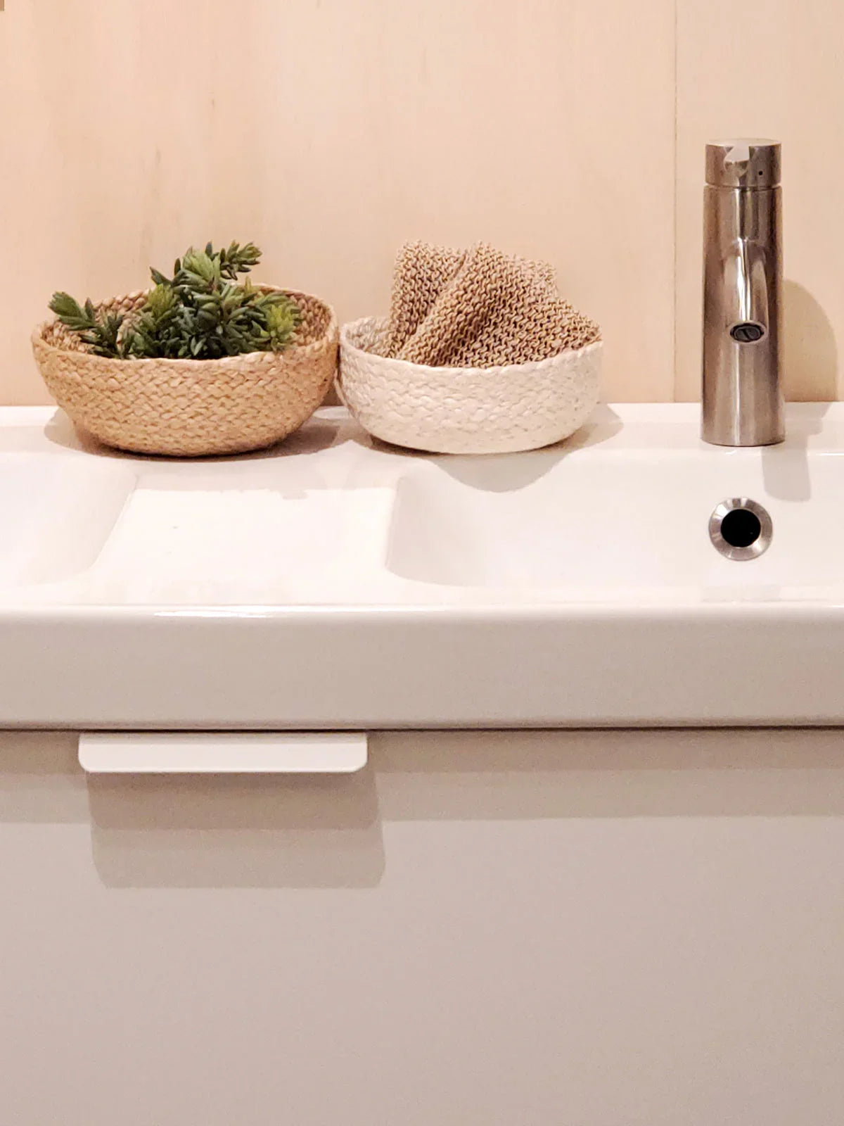 Natural woven baskets with greenery and sponges on a modern white sink, Qu!rk Boutique decor