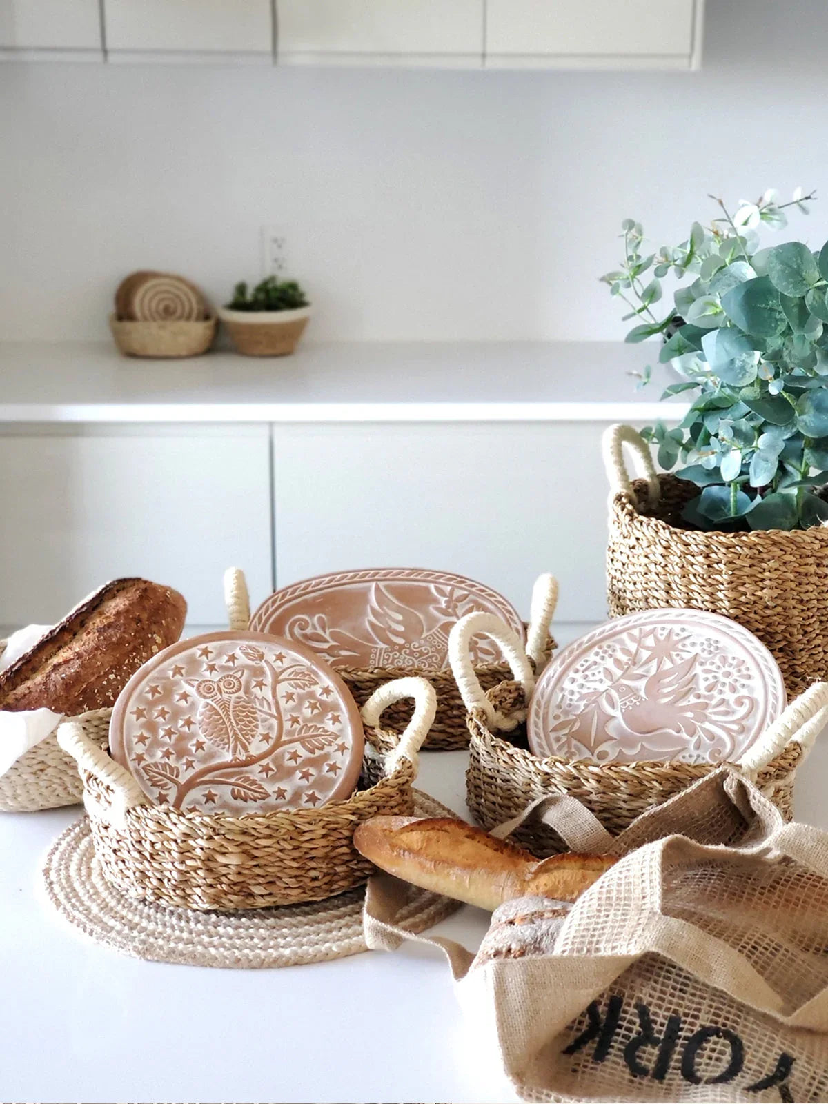 woven bread warmer baskets with embossed ceramic heat tiles and fresh bread on a white kitchen counter