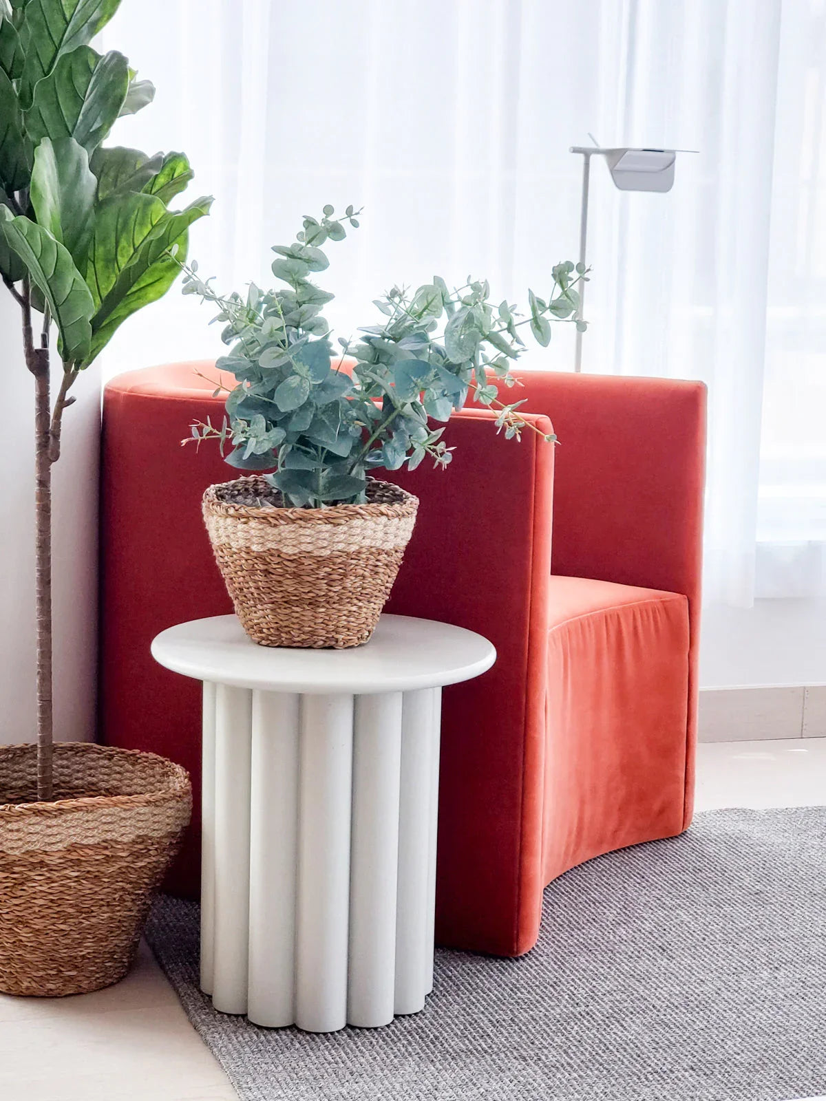Modern living room with orange velvet chair, woven planter on white round table, and leafy plant