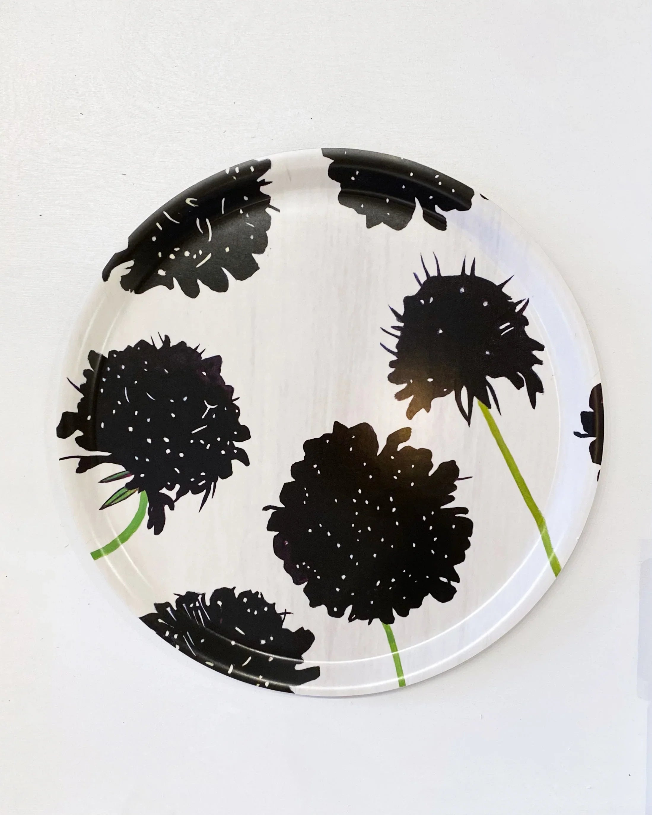 Round white serving tray with bold black floral prints and green stems, aerial view