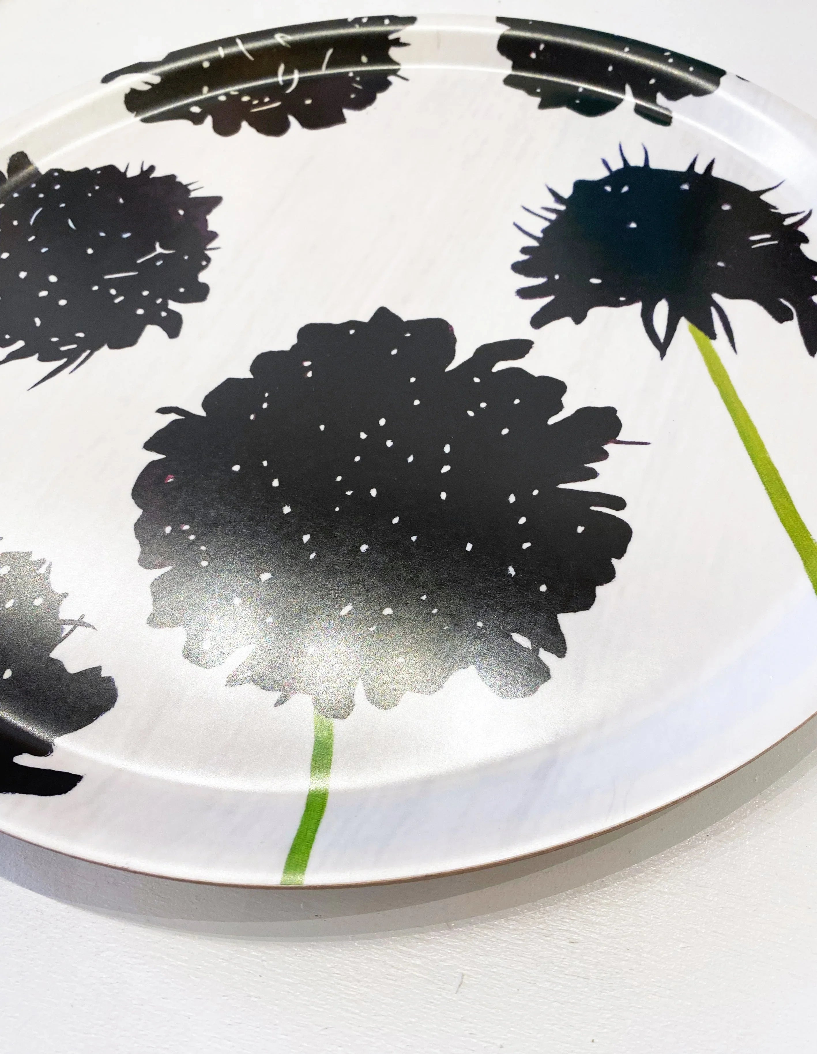 Round serving tray with black scabiosa flower prints and green stems on white background