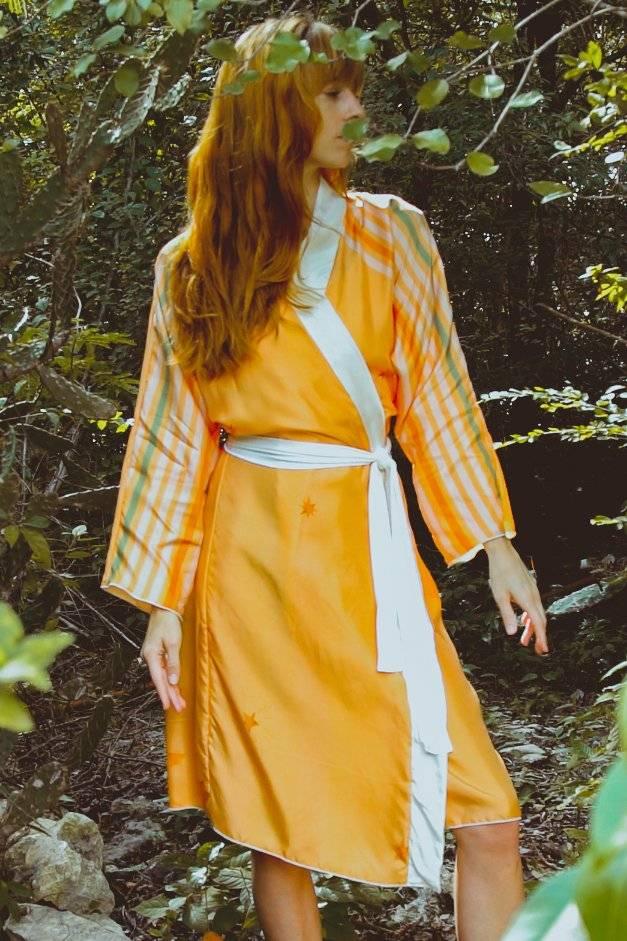 Woman in orange and white wrap dress with striped sleeves standing in forest greenery