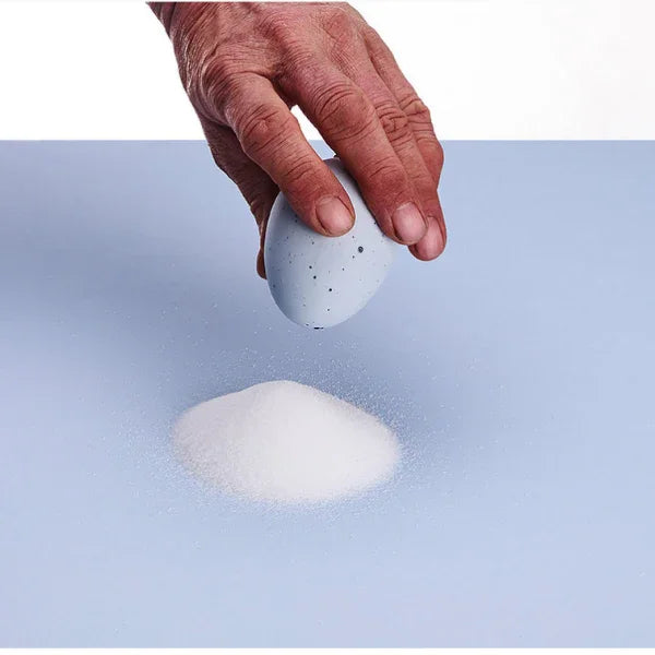 Hand holding egg-shaped shaker sprinkling salt onto blue surface, Qu!rk Boutique gift shop