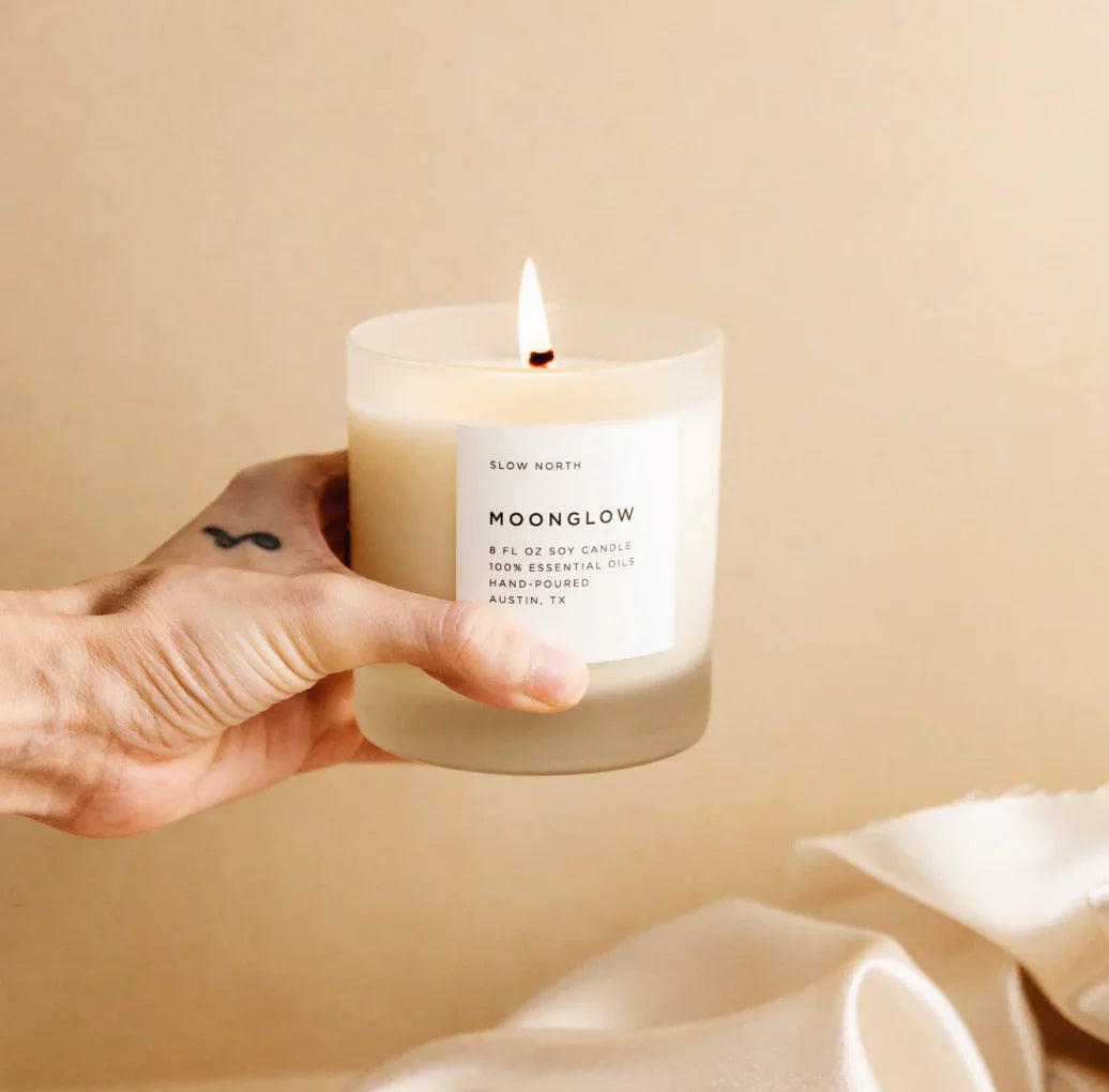Hand holding a lit Moonglow soy candle labeled with essential oils from Slow North, Austin TX