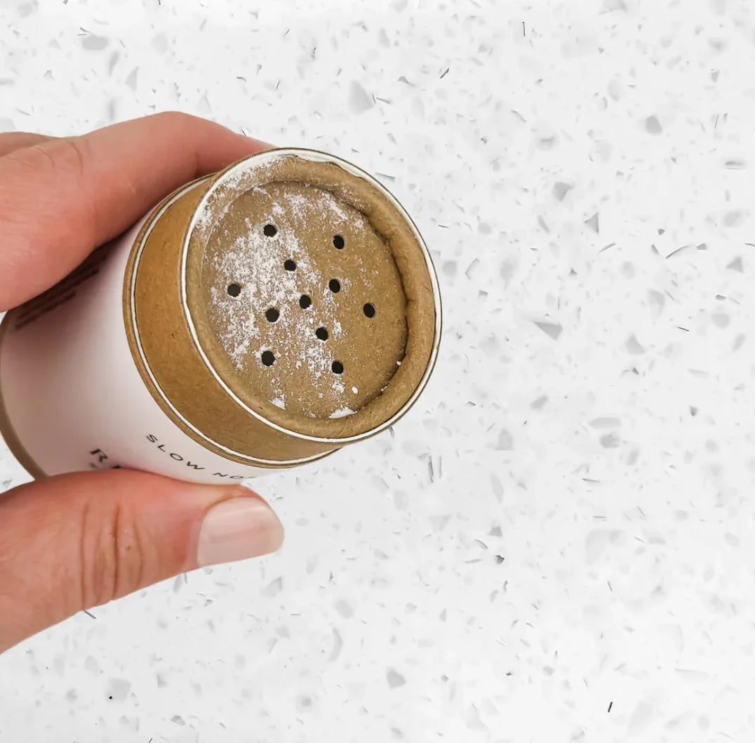 Hand holding a brown paper spice shaker with powder inside on white terrazzo surface