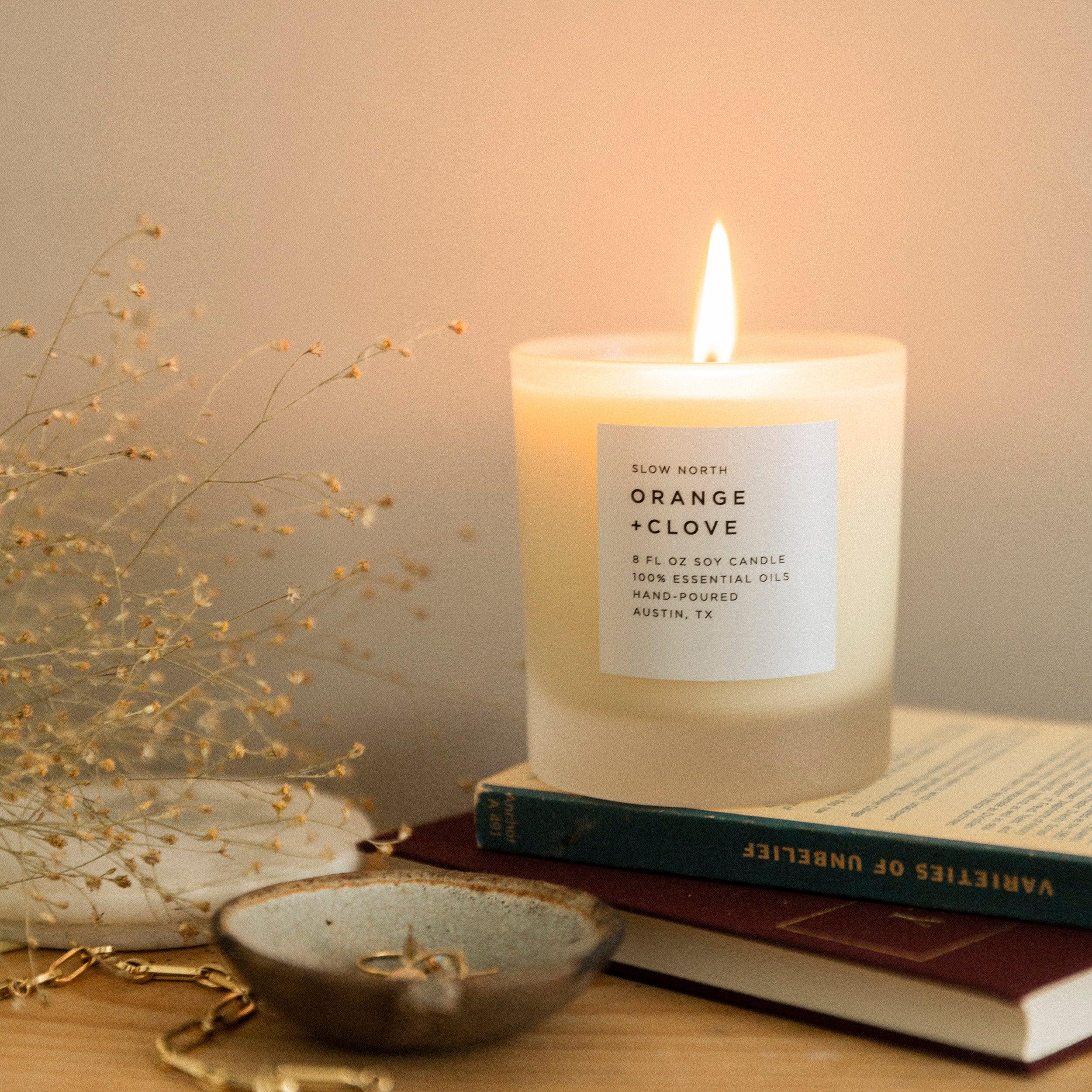 Lit Slow North orange and clove soy candle on books with dried flowers and ceramic dish